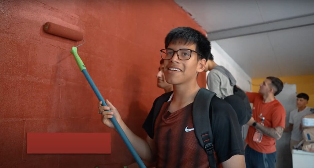 Niño con lentes pintando una pared de rojo